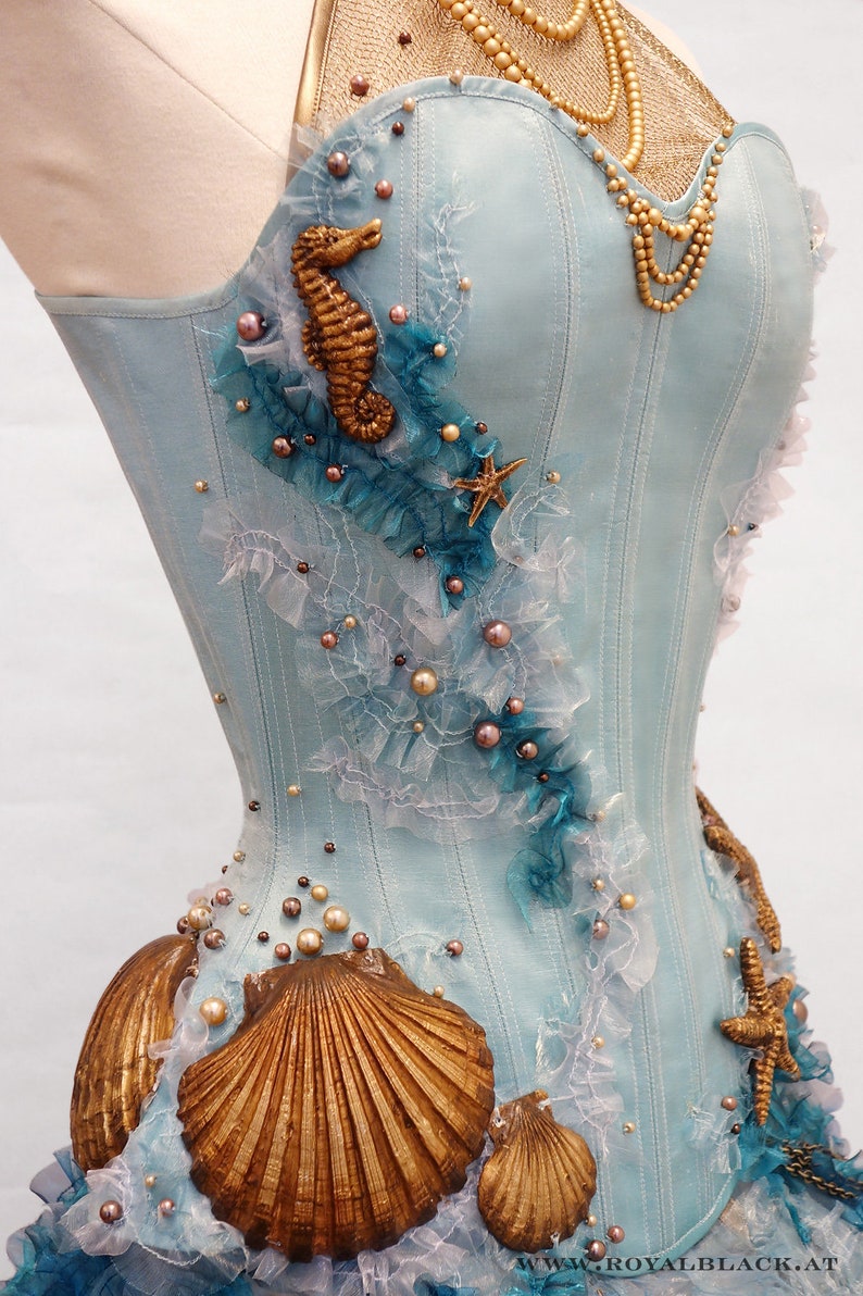 Puede incluir: Un cors&eacute; azul claro con un caballito de mar, conchas y estrellas de mar como adornos. El cors&eacute; est&aacute; decorado con perlas y encaje.