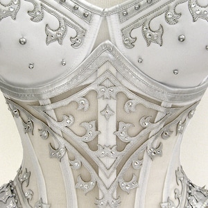 May include: A white corset with silver detailing and rhinestones. The corset has a lace-up back and a busk closure in the front.