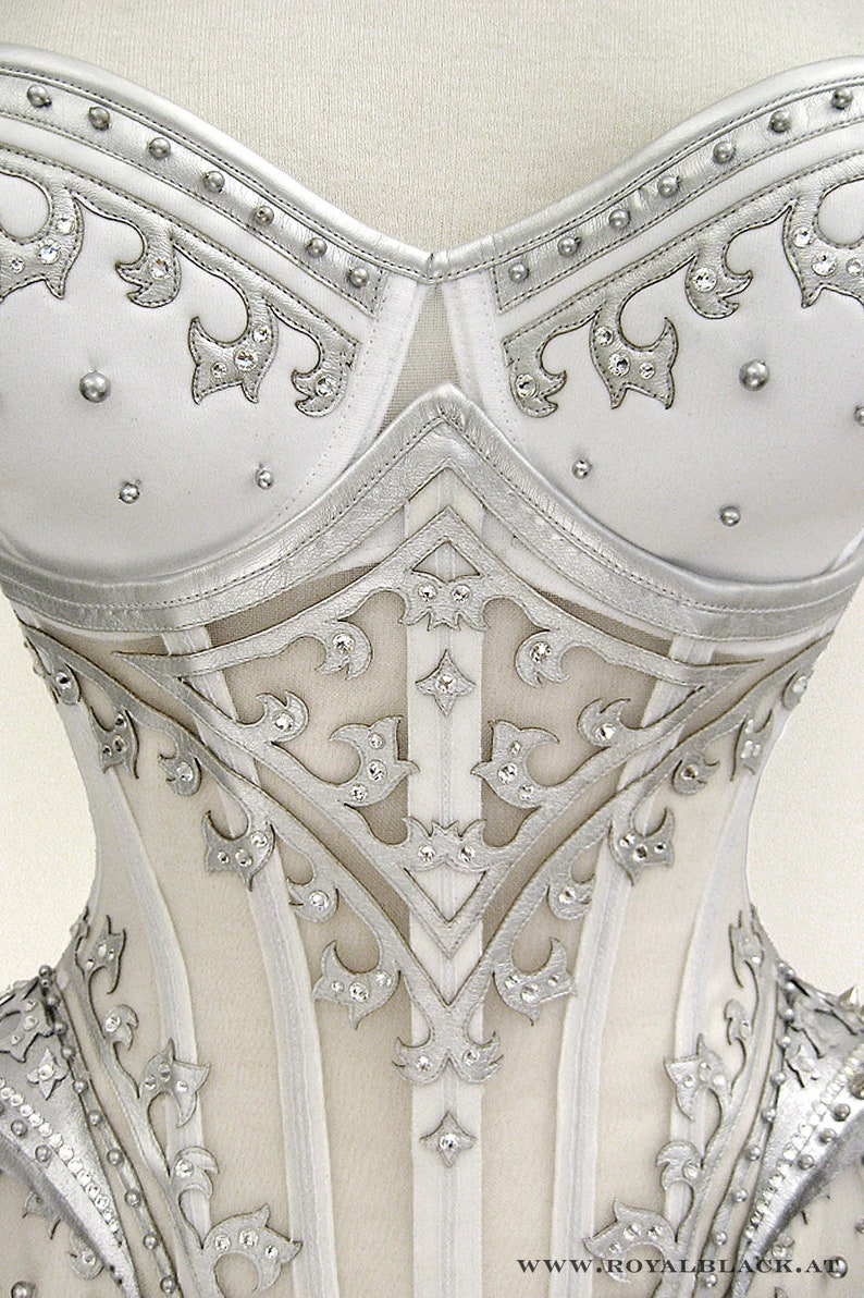May include: A white corset with silver detailing and rhinestones. The corset has a lace-up back and a busk closure in the front.