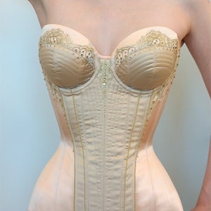 May include: A beige strapless corset with gold lace trim and rhinestones. The corset has a boned structure and a smooth satin finish.