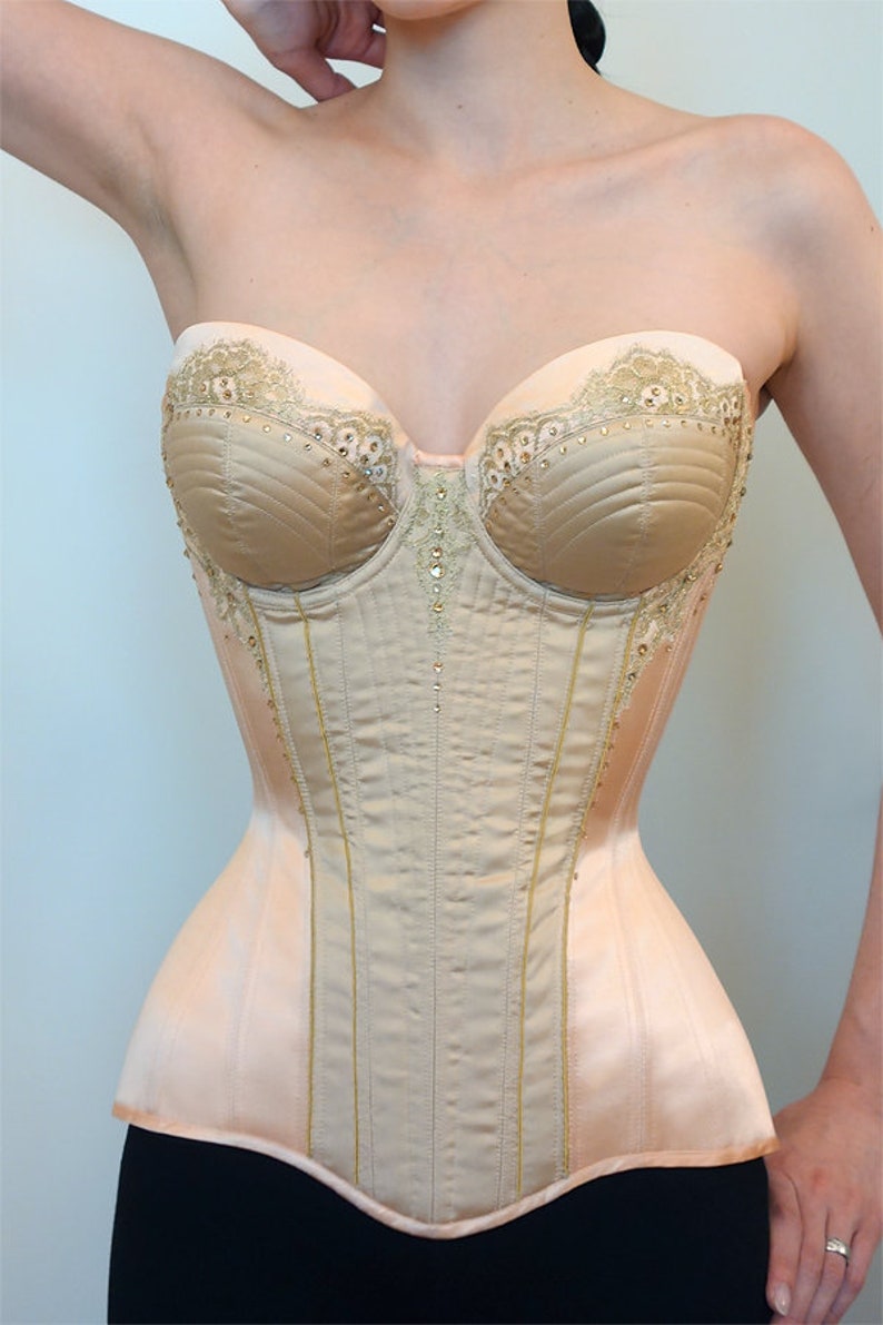 May include: A beige strapless corset with gold lace trim and rhinestones. The corset has a boned structure and a smooth satin finish.