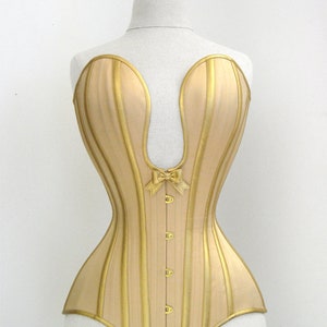Op de afbeelding: Een gouden corset met verticale strepen en een strik in het midden. Het corset heeft een puntige halslijn en een geboned structuur.