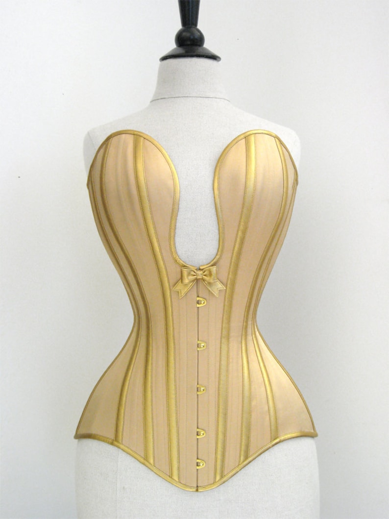 Op de afbeelding: Een gouden corset met verticale strepen en een strik in het midden. Het corset heeft een puntige halslijn en een geboned structuur.