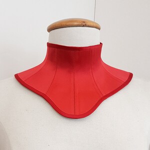 May include: A red satin choker with a curved neckline and a seam down the center.