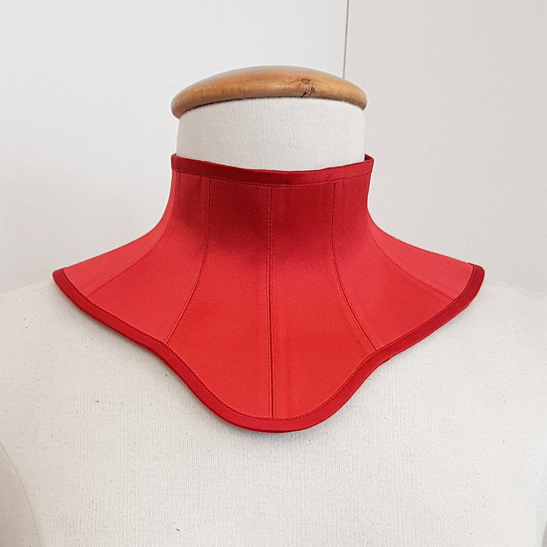 May include: A red satin choker with a curved neckline and a seam down the center.