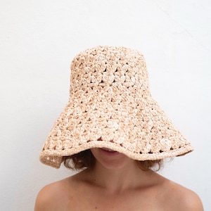 Può includere: Un cappello a secchiello all'uncinetto color beige caratterizzato da un motivo ripetitivo a forma di stella su tutta la calotta e da una tesa larga leggermente ondulata. Il cappello è realizzato in fibra testurizzata chiara con trama regolare.