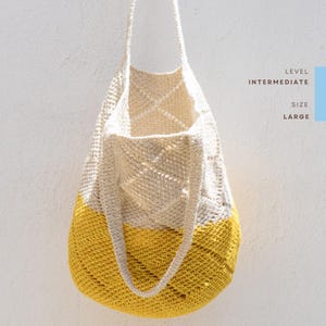 Könnte beinhalten: Eine große, zweifarbige Häkeltasche. Die obere Hälfte ist cremefarben, die untere Hälfte ist gelb. Die Tasche hat lange Henkel und hängt an einer weißen Wand. Der Text auf der Seite lautet "Level Intermediate Size Large".