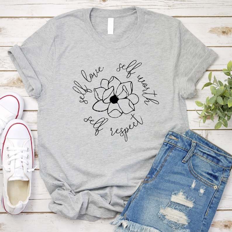 May include: A gray t-shirt with a black floral design and the text "self love self worth self respect" around the flower.