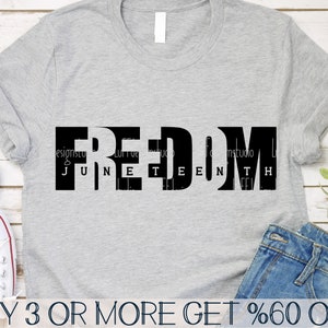 May include: A grey t-shirt with black text that reads "FREEDOM JUNETEENTH". The shirt is lying on a wooden surface with a pair of blue jeans and a pair of white trainers.