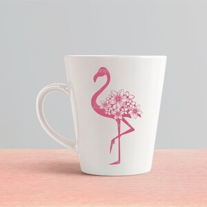 May include: A white ceramic mug with a pink flamingo silhouette design. The flamingo has flowers on its back.