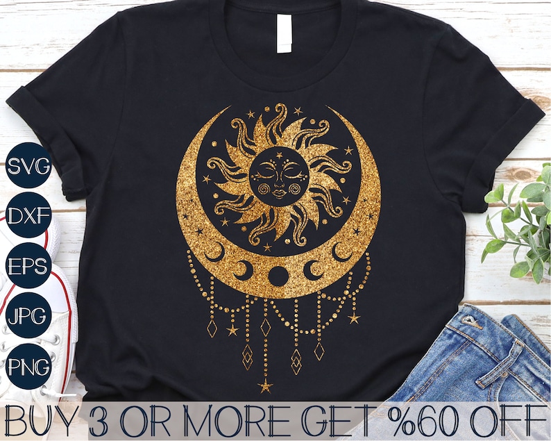 May include: A black t-shirt with a gold glitter design of a sun and moon with a crescent moon and stars. The design has a bohemian style with a beaded chain hanging from the bottom.