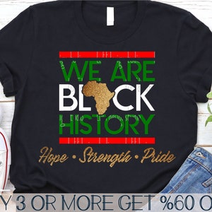 May include: Black t-shirt with a red, white, and green graphic that says "We Are Black History" with a gold outline of the continent of Africa. The text "Hope - Strength - Pride" is written in gold below the graphic.