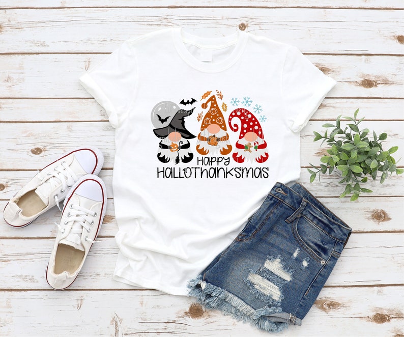 May include: White t-shirt with a graphic of three gnomes wearing hats and holding pumpkins. The text "Happy Hallothanksmas" is printed below the gnomes.