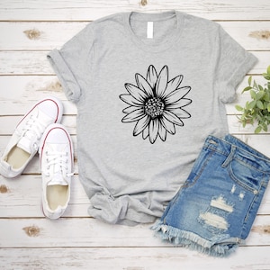 May include: A gray t-shirt with a black daisy graphic. The t-shirt is paired with denim shorts and white sneakers.