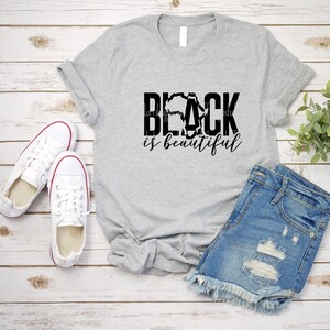 May include: A grey t-shirt with the text "Black is beautiful" in black lettering. The "Black" text is stylised with an outline of the African continent.