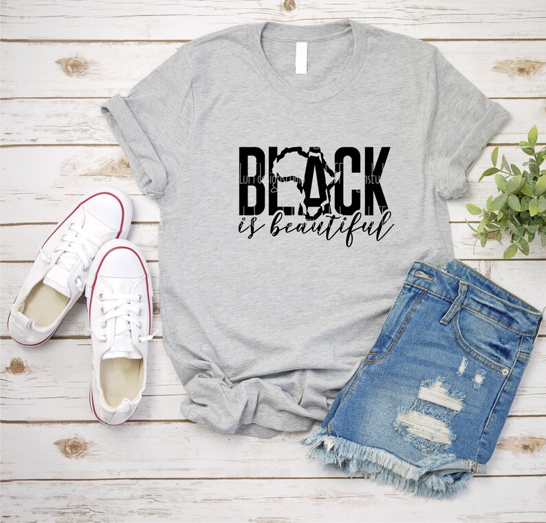 May include: A grey t-shirt with the text "Black is beautiful" in black lettering. The "Black" text is stylised with an outline of the African continent.