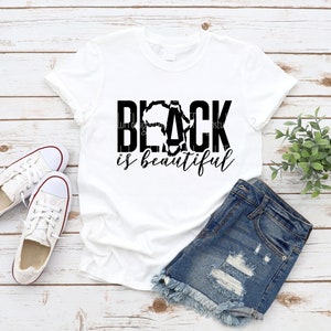 May include: White t-shirt with black text that reads "Black is beautiful" with a stylized outline of the continent of Africa in the middle of the word "Black".