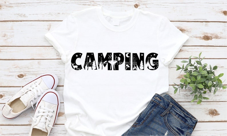 Op de afbeelding: Wit T-shirt met zwarte tekst die "CAMPING" zegt met camping-silhouetten in de letters.