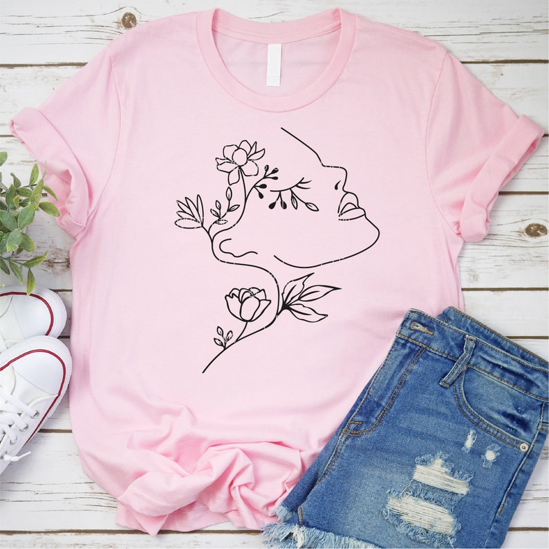 May include: A pink t-shirt with a black line drawing of a face with flowers growing from the eye and cheek.