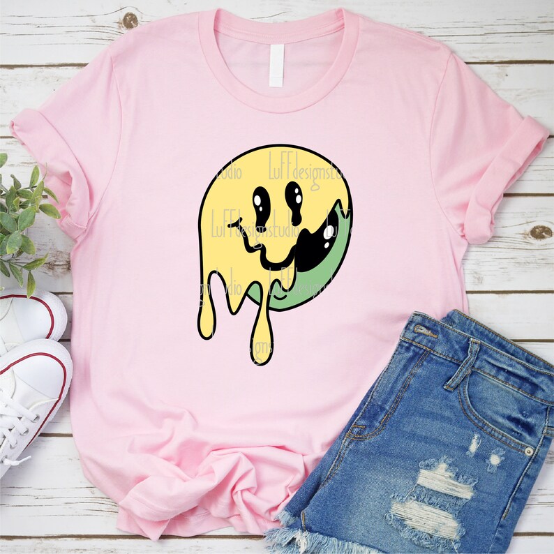 May include: A pink t-shirt featuring a yellow and green dripping smiley face graphic. The graphic has a black outline and the smiley face has black eyes and a black mouth.