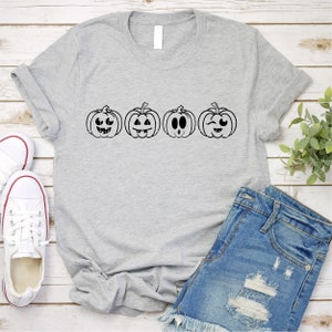 May include: A gray t-shirt with a row of four black and white pumpkin faces with different expressions. The pumpkins are all the same size and shape.