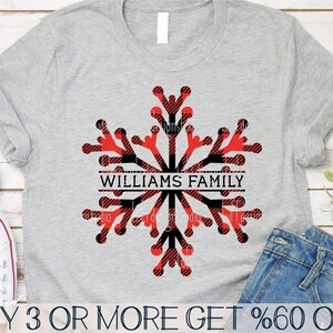 Pode incluir: Uma camiseta cinza com um design de floco de neve xadrez vermelho e preto. O floco de neve tem o texto "WILLIAMS FAMILY" em uma faixa preta.