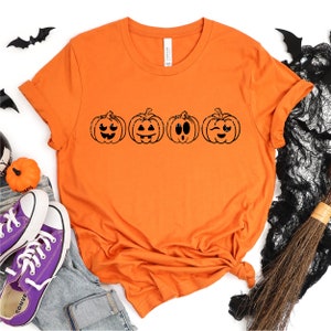 May include: Orange t-shirt with a row of four black pumpkin faces with different expressions.