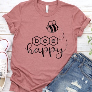 May include: A pink t-shirt with a black bee and honeycomb design. The text "bee happy" is printed on the shirt.