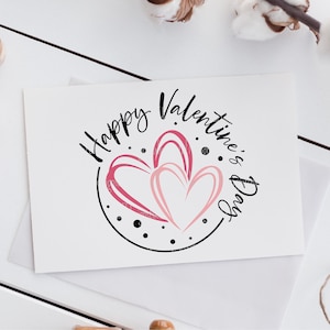 Puede incluir: Una tarjeta blanca con un c&iacute;rculo negro y el texto "Happy Valentine's Day" en letra negra. Dentro del c&iacute;rculo hay dos corazones rosas.
