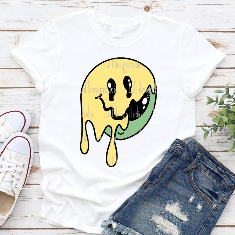 May include: A white t-shirt featuring a yellow and green dripping smiley face graphic. The graphic has black outlines and black eyes.
