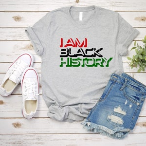 May include: A gray t-shirt with the text "I AM BLACK HISTORY" in black, red, and green letters.