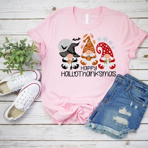 May include: Pink t-shirt with a graphic of three gnomes dressed for Halloween, Thanksgiving, and Christmas. The text "Happy Hallothanksmas" is printed below the gnomes.