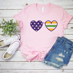 May include: Pink t-shirt with a purple heart-shaped sunglasses design. One heart has the American flag and the other has the Irish flag.
