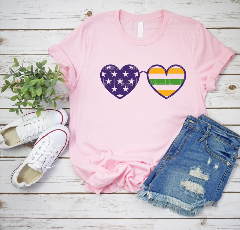 May include: Pink t-shirt with a purple heart-shaped sunglasses design. One heart has the American flag and the other has the Irish flag.