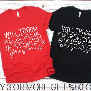 May include: Two t-shirts with a Christmas theme. The red shirt says "Will trade sister for presents" with snowflakes and a gift box. The black shirt says "Will trade brother for presents" with snowflakes and a gift box.