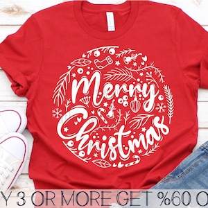 May include: Red t-shirt with a white circle design that says "Merry Christmas" surrounded by festive elements like snowflakes, stars, candy canes, and ornaments.