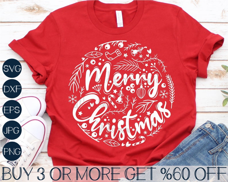 May include: Red t-shirt with a white circle design that says "Merry Christmas" surrounded by festive elements like snowflakes, stars, candy canes, and ornaments.