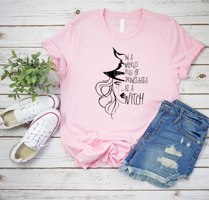 Peut inclure: T-shirt rose avec un graphique noir d'une sorci&egrave;re avec le texte "Dans un monde plein de princesses... sois une sorci&egrave;re".