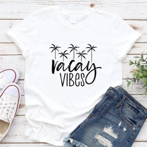 May include: White t-shirt with a black graphic of palm trees and the text "vacay vibes".