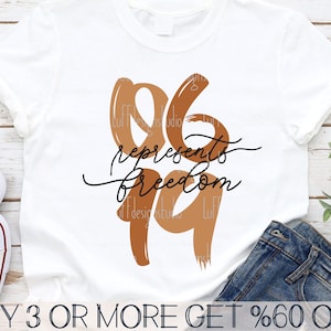 May include: A white t-shirt with a brown and orange graphic design that says "06 represents freedom" with the numbers in a brushstroke style.