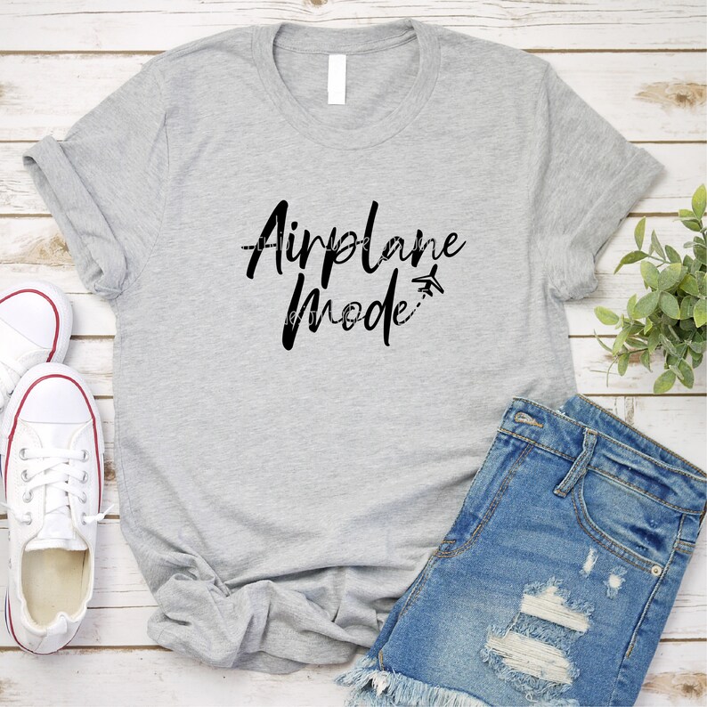 May include: A gray t-shirt with the text "Airplane Mode" in black lettering. The text is stylized with a small airplane icon and a dashed line.