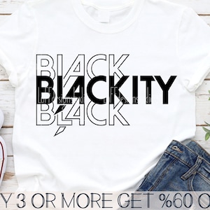 May include: A white t-shirt with a black graphic design that says "BLACK BLACKITY BLACK" in a layered, stylized font. The text is centered on the shirt. The shirt is on a wooden surface with a pair of jeans and a plant in the background. The text "BUY 3 OR MORE GET %60 OFF" is at the bottom of the image.