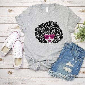 May include: Gray t-shirt with a black and white graphic of a woman with an afro. The graphic includes the words "Magic", "Strong", "Queen", "Love", and "Black".