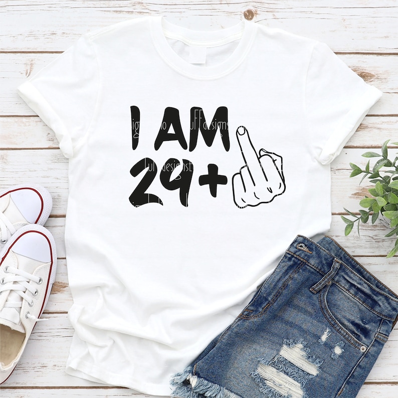 May include: White t-shirt with black text that reads "I AM 29+" and a black silhouette of a middle finger.