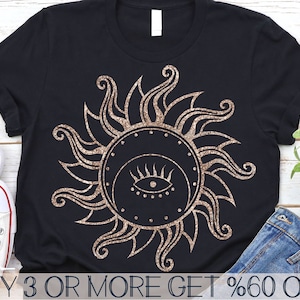 May include: A black t-shirt with a gold glitter design of a sun with an eye in the center. The text "BUY 3 OR MORE GET %60 OFF" is at the bottom of the shirt.