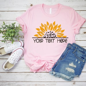 May include: A pink t-shirt with a yellow sunflower design featuring a black and white leopard print in the center. The text "YOUR TEXT HERE" is printed below the sunflower.