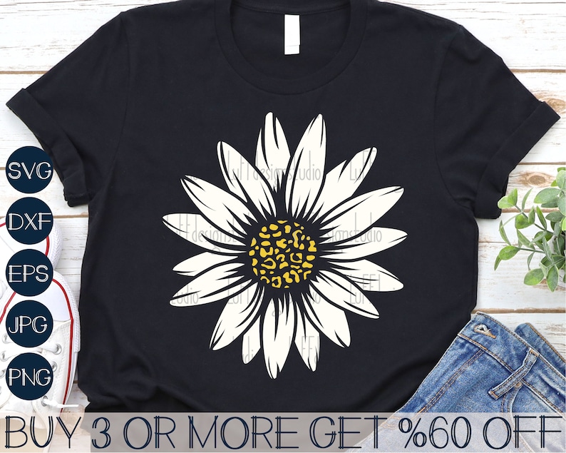 Op de afbeelding: Een zwart T-shirt met een witte madeliefje met een geel en bruin luipaardprint in het midden. De tekst "BUY 3 OR MORE GET %60 OFF" staat onderaan het shirt.