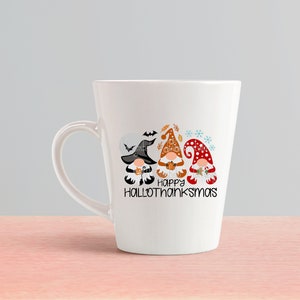 May include: White ceramic coffee mug with a design of three gnomes wearing hats and holding pumpkins. The gnomes are in a line and the text "Happy Hallothanksmas" is below them.