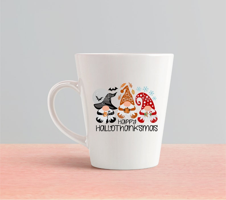 May include: White ceramic coffee mug with a design of three gnomes wearing hats and holding pumpkins. The gnomes are in a line and the text "Happy Hallothanksmas" is below them.