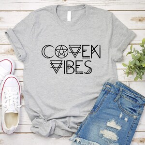 May include: Gray t-shirt with black text that reads "Coven Vibes" with a pentagram and other geometric shapes.